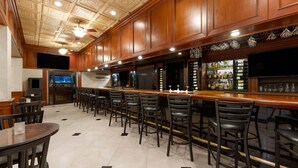 A bar area with wooden cabinets, a long counter, and multiple bar stools. - Wyndham Riverfront Little Rock (North Little Rock)