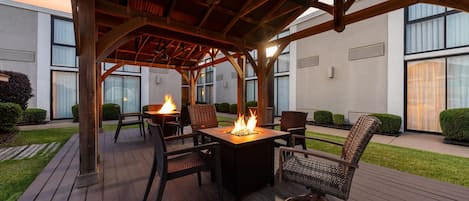 Un patio exterior con una pérgola de madera, un brasero y sillas de mimbre.