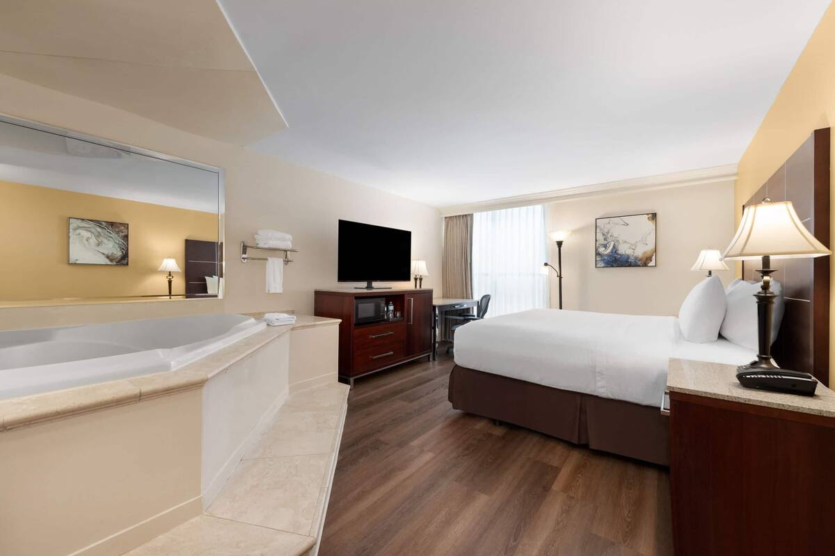A hotel room with a large bed, a desk, a television, a bathroom with a bathtub, and a large mirror.
