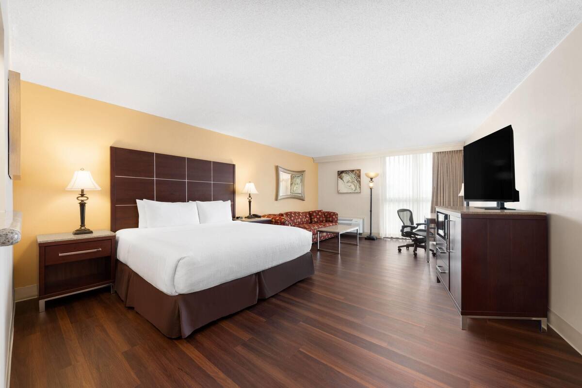 A hotel room with a large bed, a desk, a chair, a television, and a sofa.