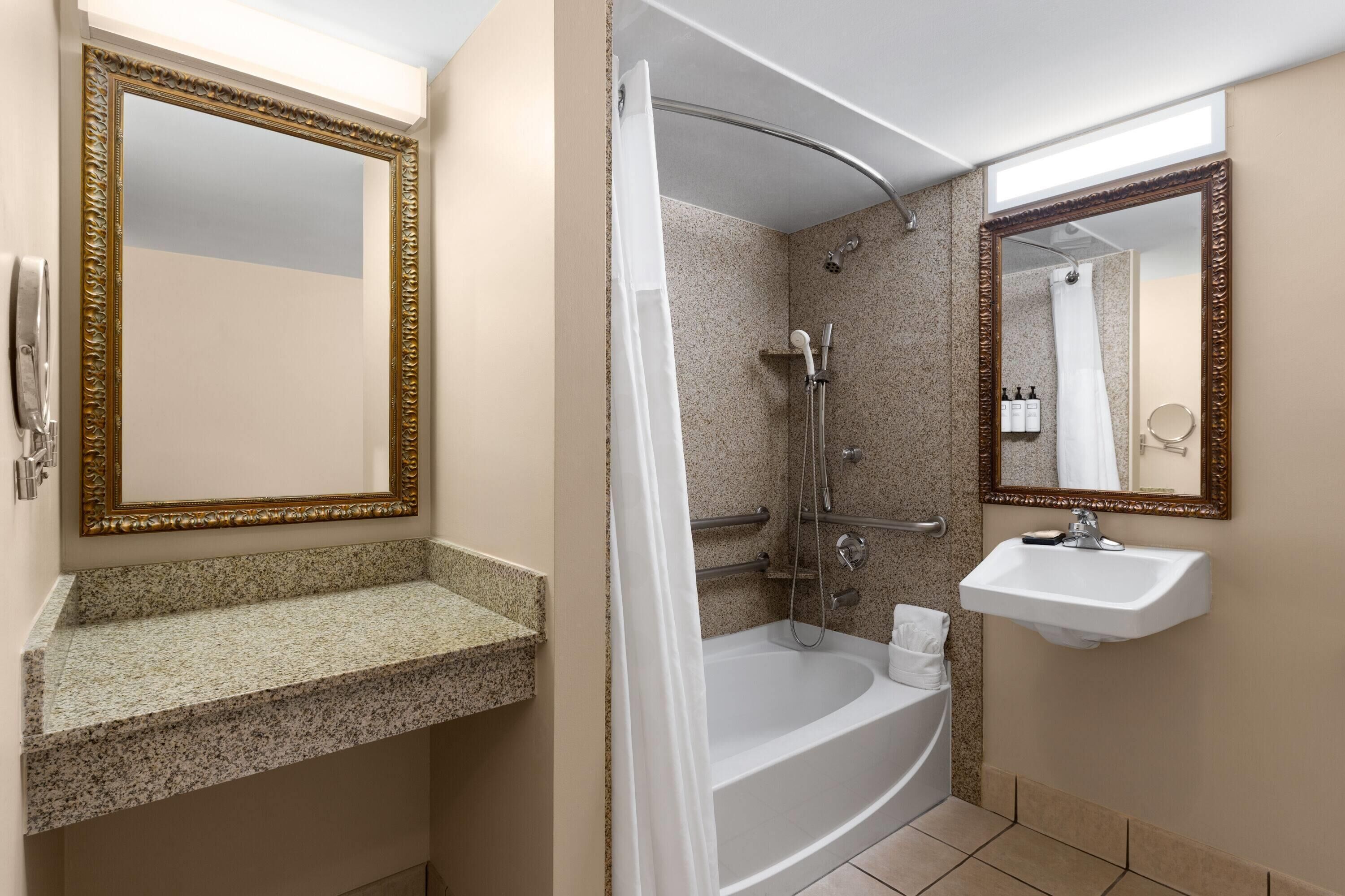 Ein Badezimmer mit einer freistehenden Badewanne, einem Waschbecken und zwei Spiegeln mit aufwendigen Rahmen.