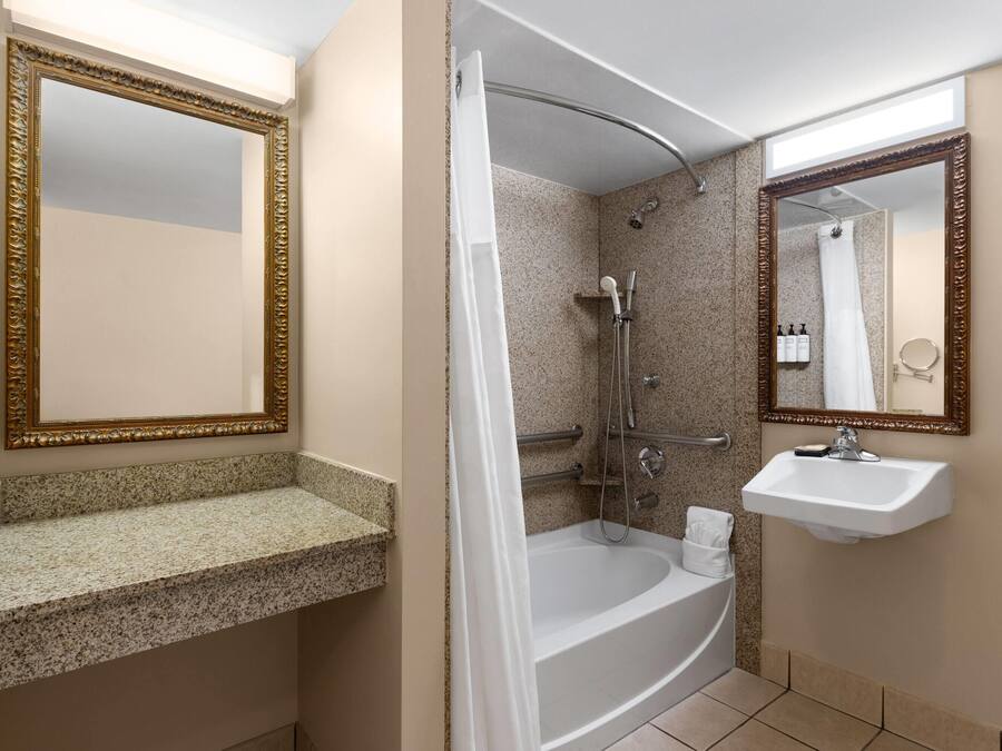 Un baño con una bañera independiente, un lavamanos y dos espejos con detalles decorativos.
