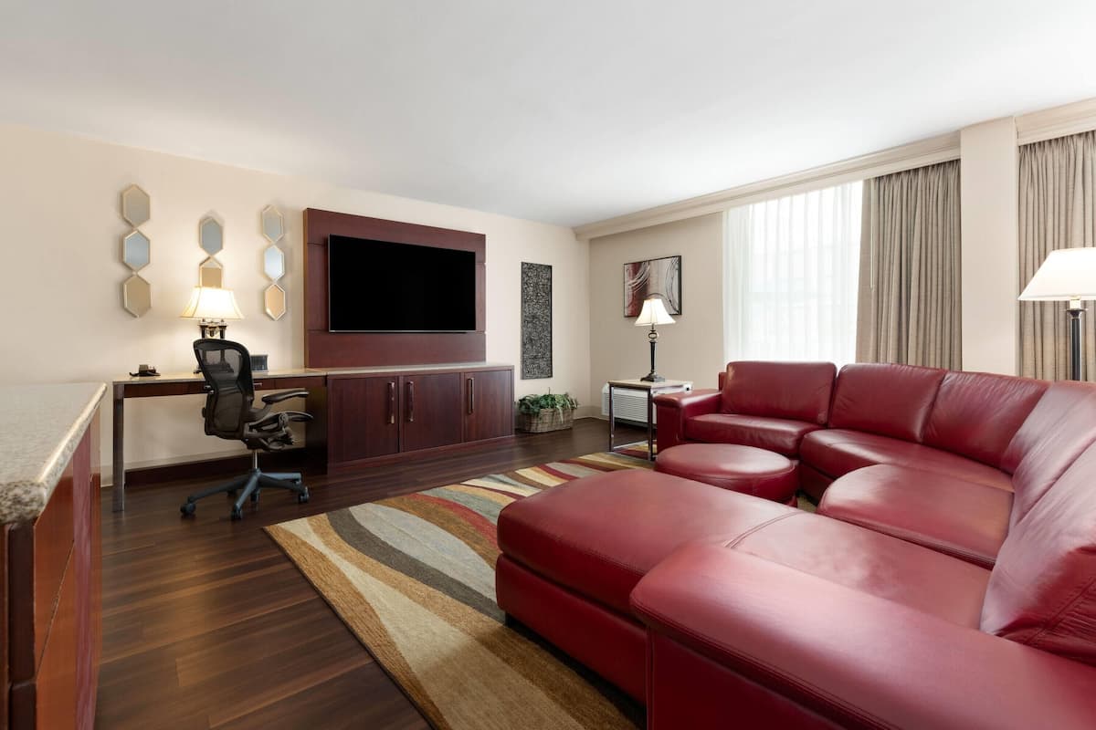A modern living room with a red leather sofa, a flat-screen TV mounted on the wall, a desk with a chair, and a patterned rug.