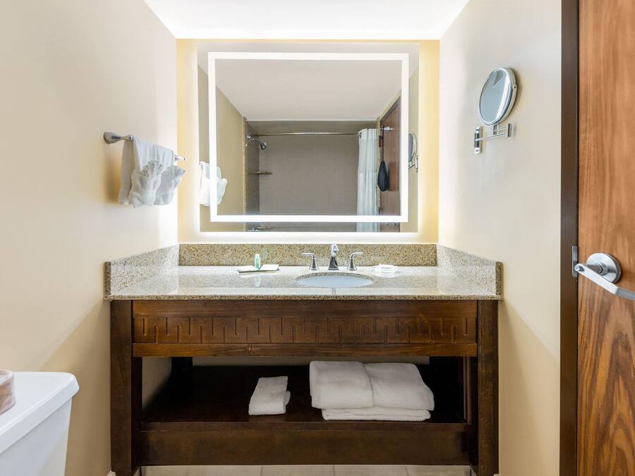 Un baño con tocador de madera, lavamanos, espejo y perchero para toallas.