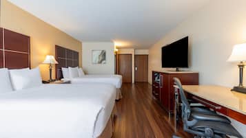 Ett hotellrum med två sängar, ett skrivbord med stolar, en TV och ett trägolv.