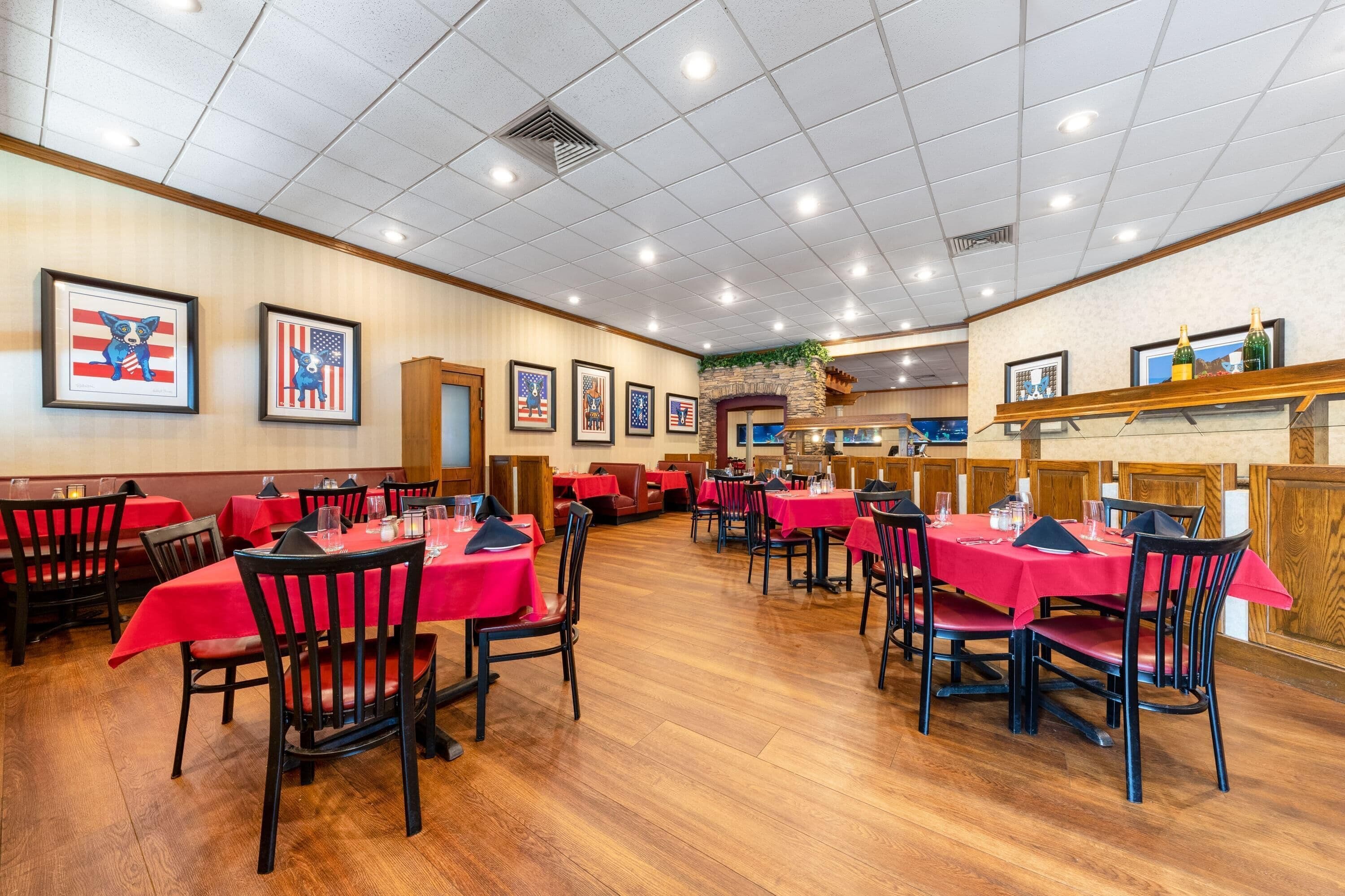 A restaurant with red tablecloths and black chairs, featuring framed American flags and a stone fireplace.