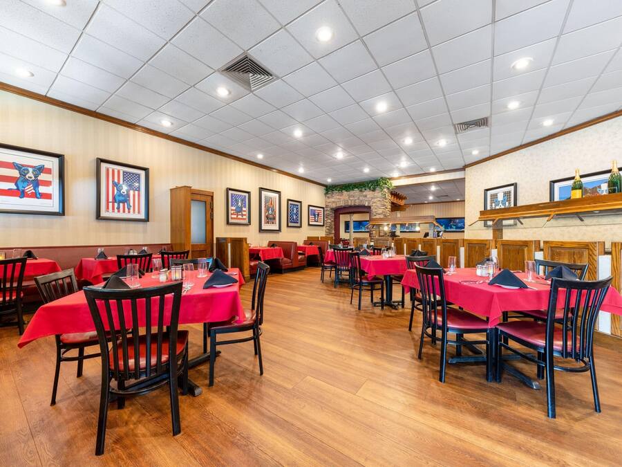 A restaurant with red tablecloths and black chairs, featuring framed American flags and a stone fireplace.