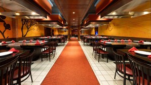 A spacious restaurant with multiple tables and chairs, a central walkway, and a modern ceiling design. - Wyndham Riverfront Little Rock (North Little Rock)