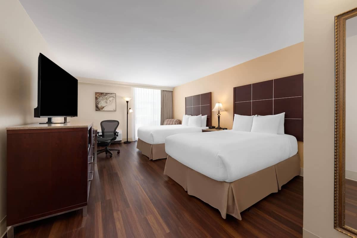A hotel room with two beds, a desk, a chair, a television, and a painting on the wall.