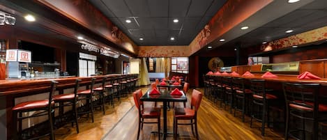 A restaurant with wooden flooring, red chairs, and a central dining table.