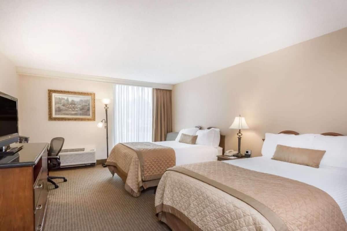 A hotel room with two beds, a desk with a computer, a TV, and a framed picture on the wall.