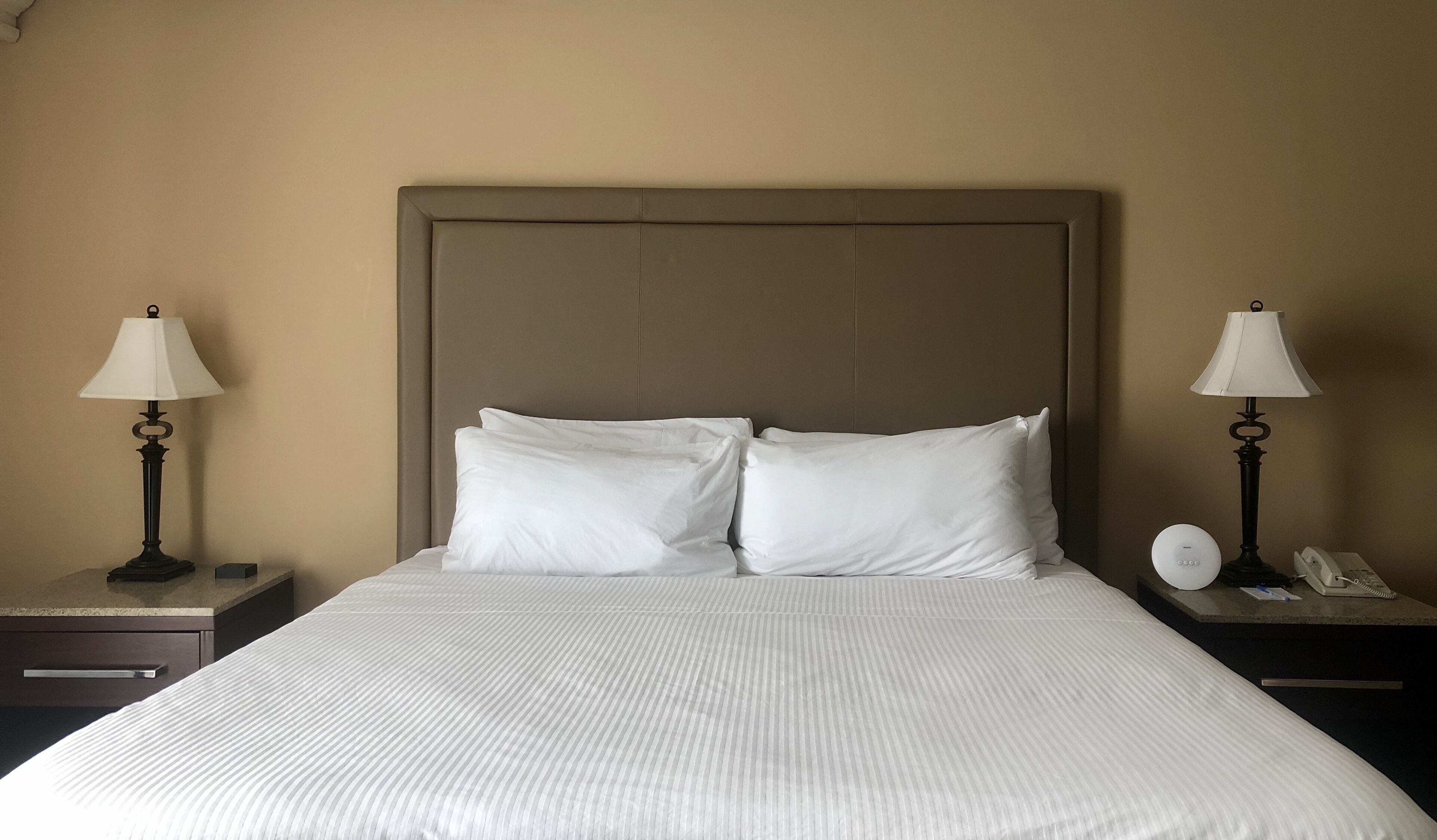 A neatly made bed with white linens, two bedside tables with lamps, and a wall-mounted telephone.