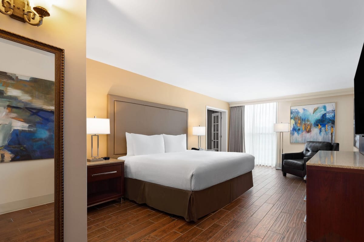 A hotel room with a large bed, a desk, a chair, and artwork on the walls.