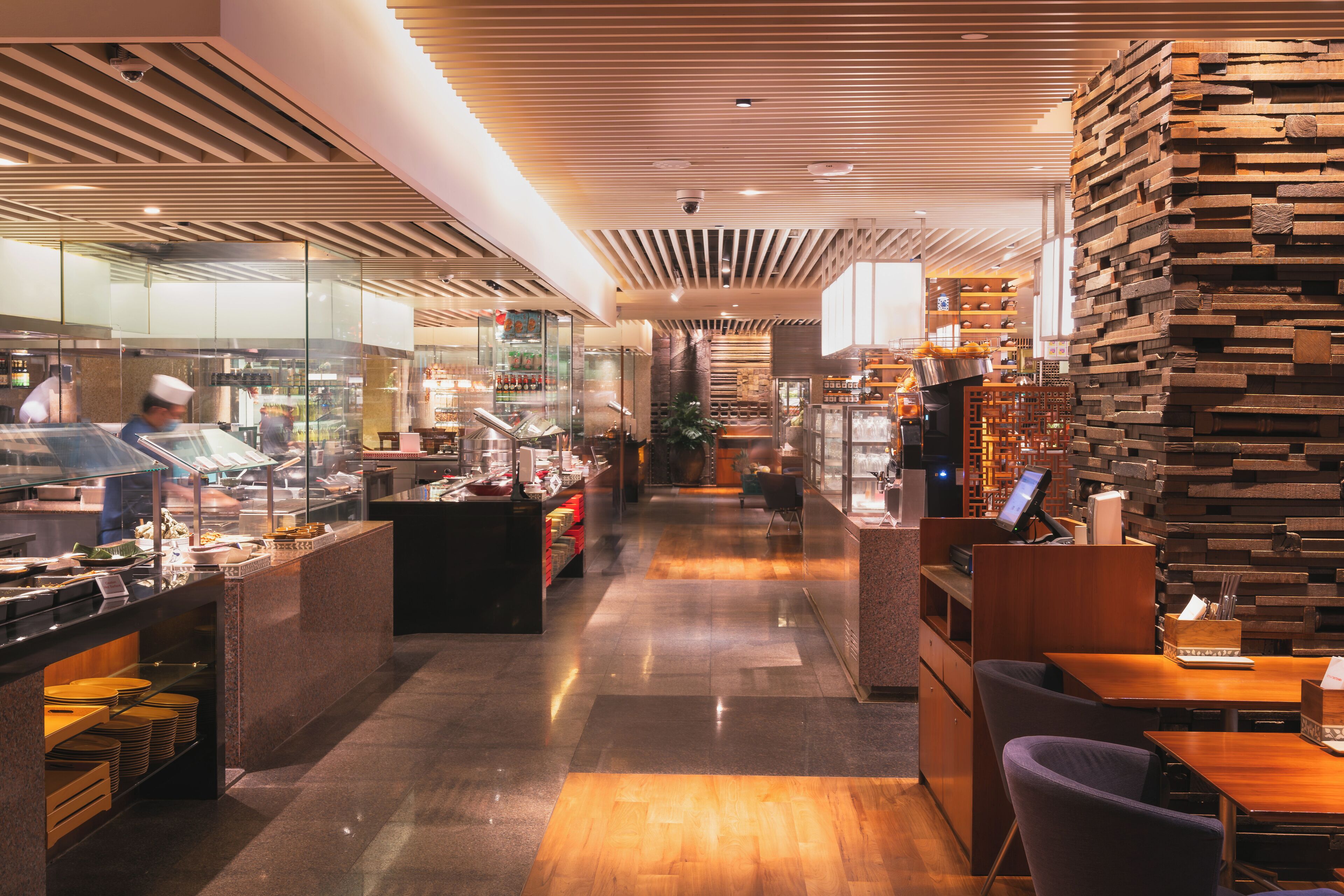 Ein modernes Restaurant-Interieur mit einer langen Theke, Sitzbereich und einer Wandgestaltung aus Holz.
