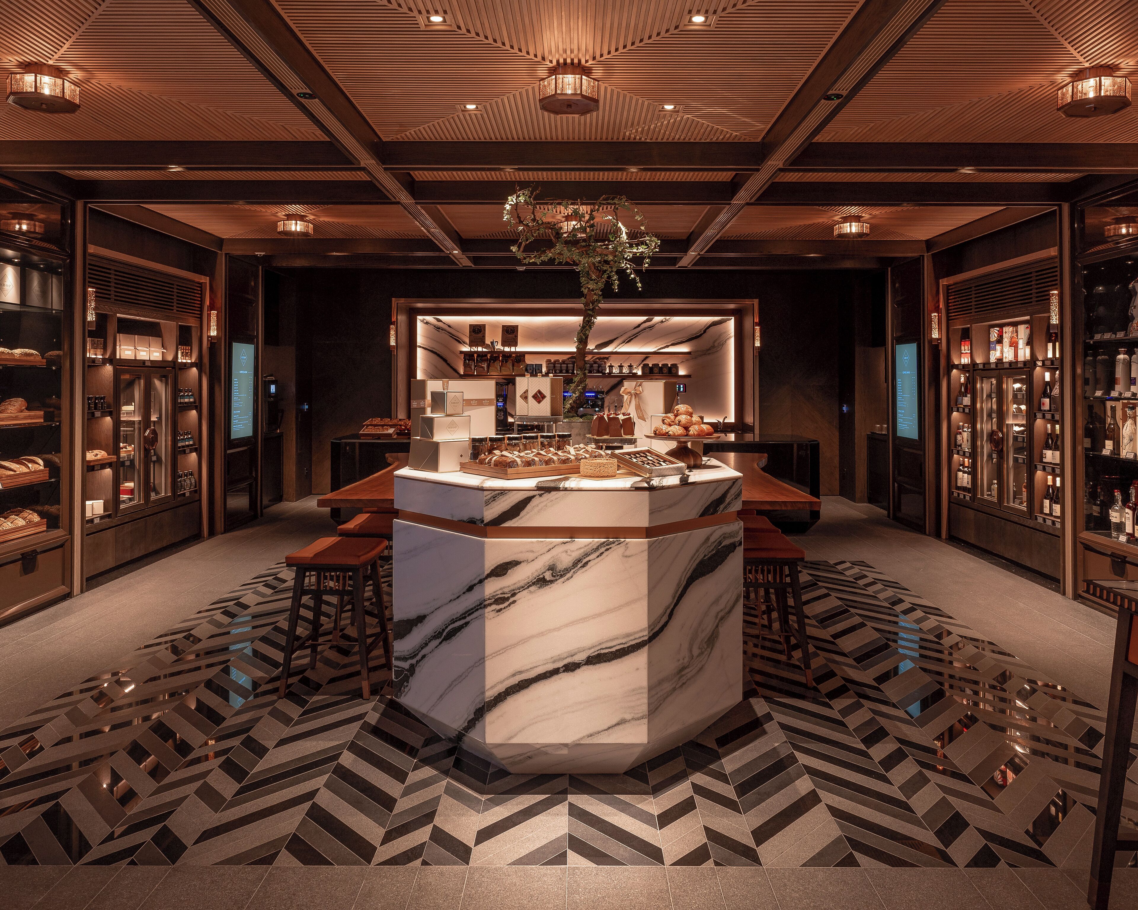 Un hall d’hôtel luxueux, avec un comptoir d’accueil en marbre, des étagères en bois ornées de bouteilles et un sol à motifs.