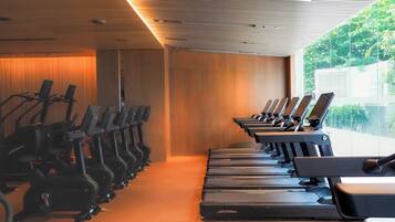 A gym with multiple treadmills and stationary bikes arranged in rows.