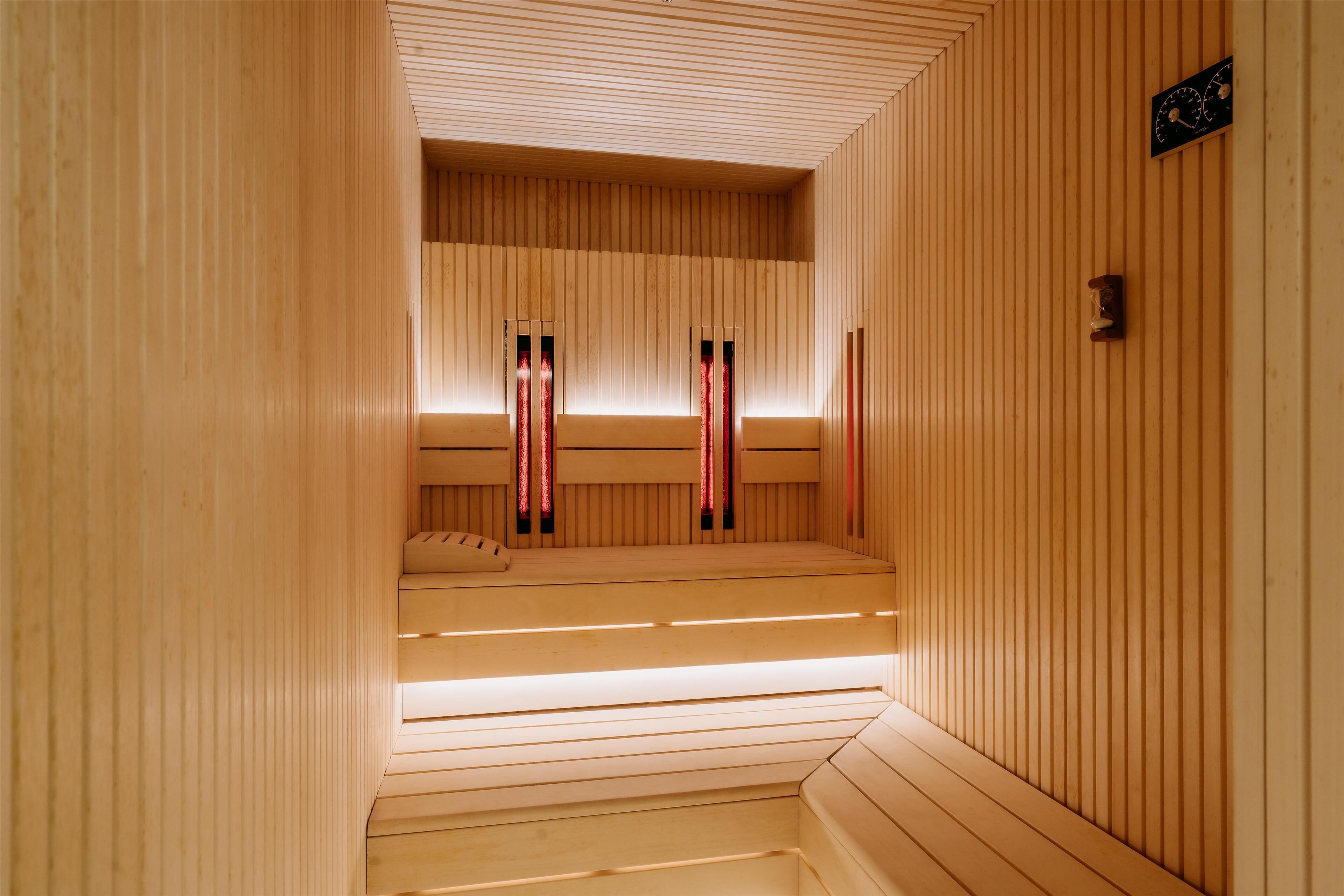 Eine Sauna mit Holzwänden und -bänken, einer Uhr und einem Fenster mit roten Vorhängen.