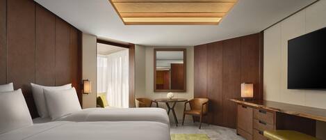 A modern hotel room with a large bed, a desk, a chair, a small table, and a TV.