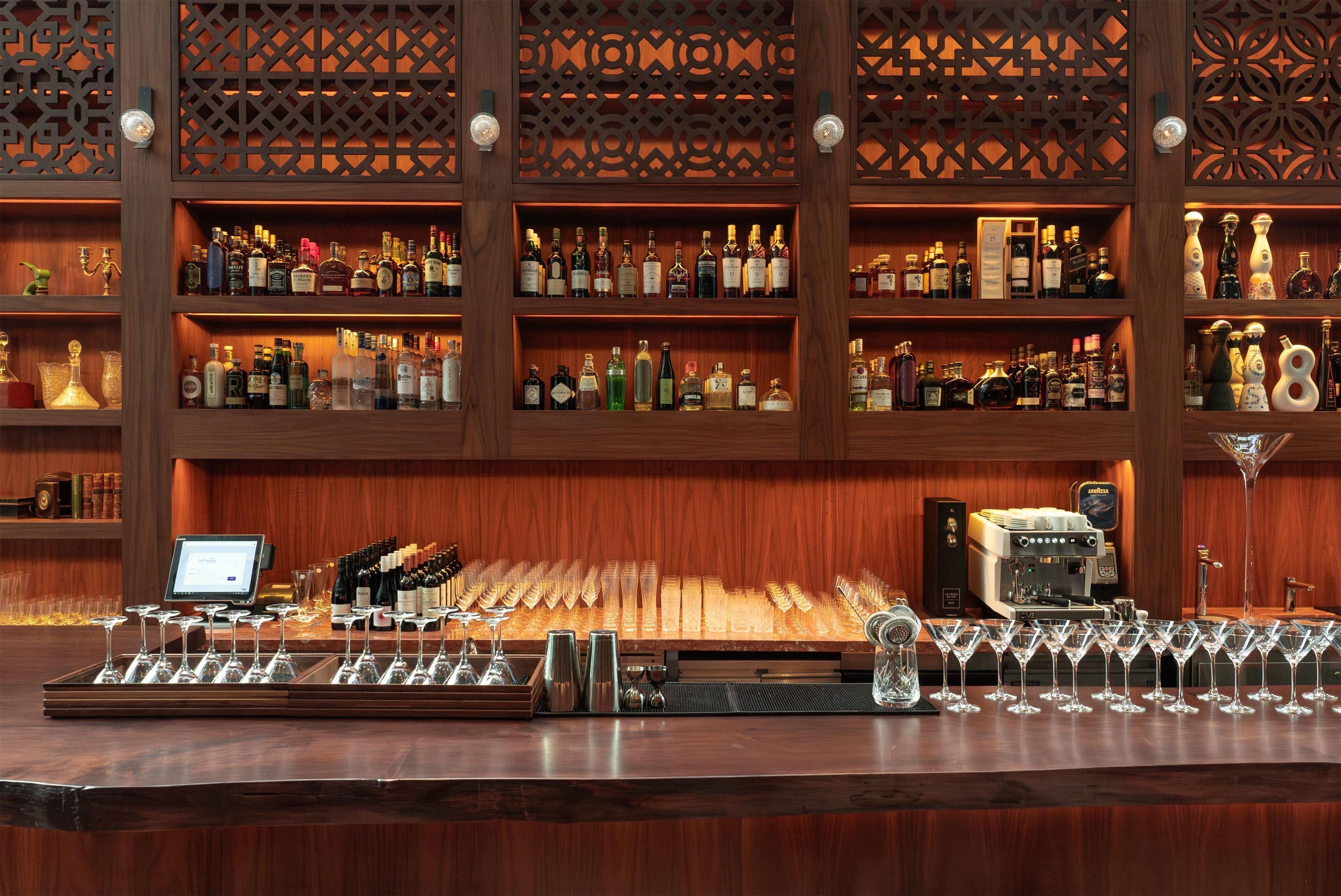 Un bar avec de nombreuses étagères remplies de bouteilles d’alcool, une machine à café et un plateau de verres à vin.