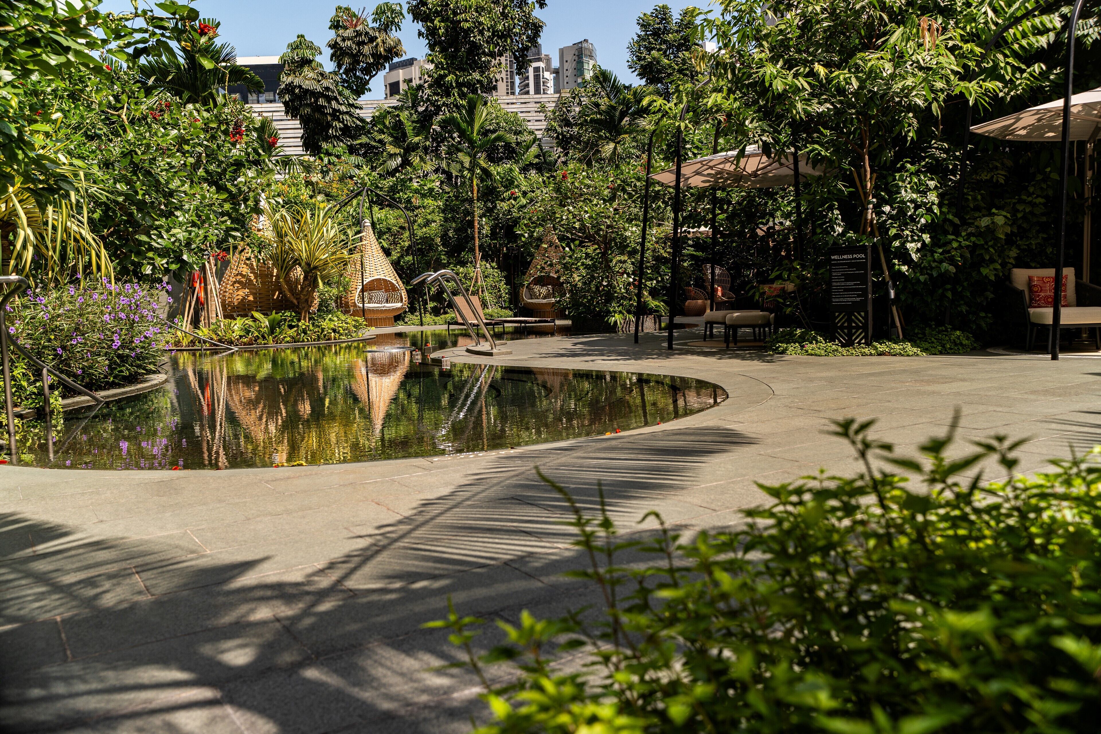 A serene outdoor area with a curved water feature, seating areas, and lush greenery.