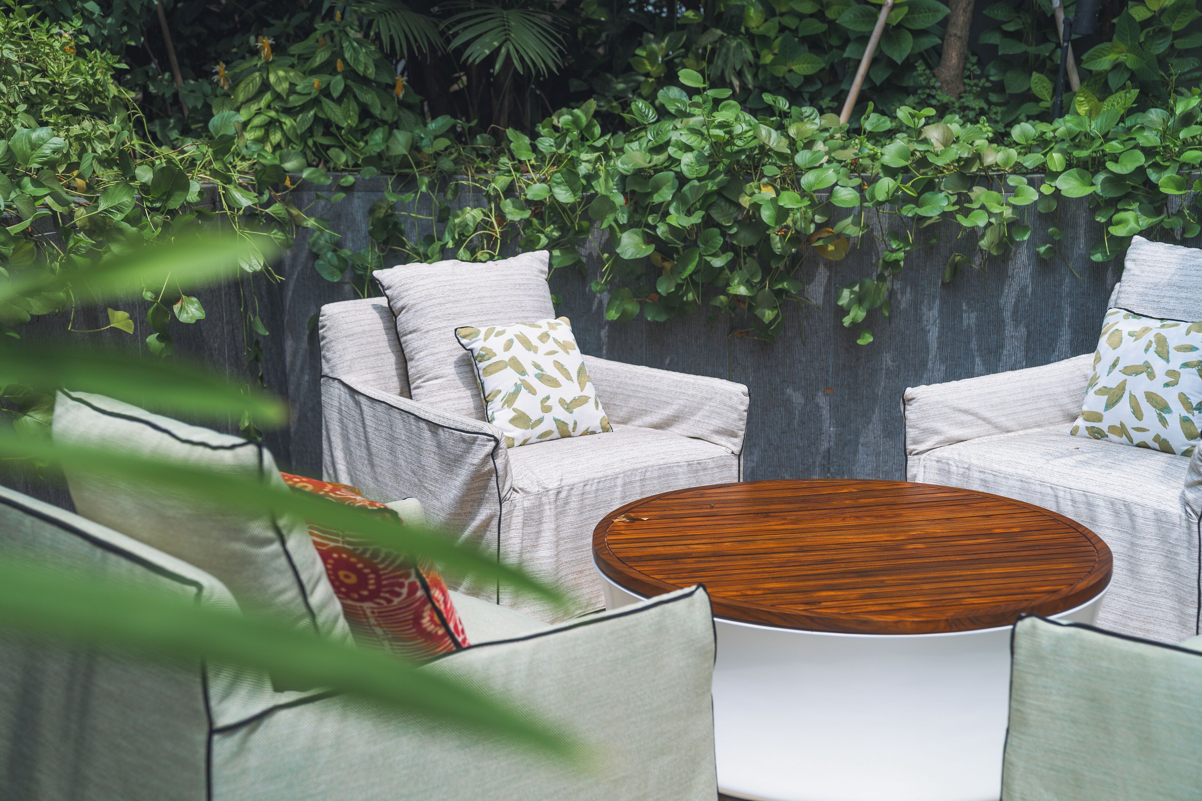 Un espacio al aire libre acogedor con dos sillones acolchados y una mesa redonda de madera, rodeado de abundante vegetación y una valla de madera.