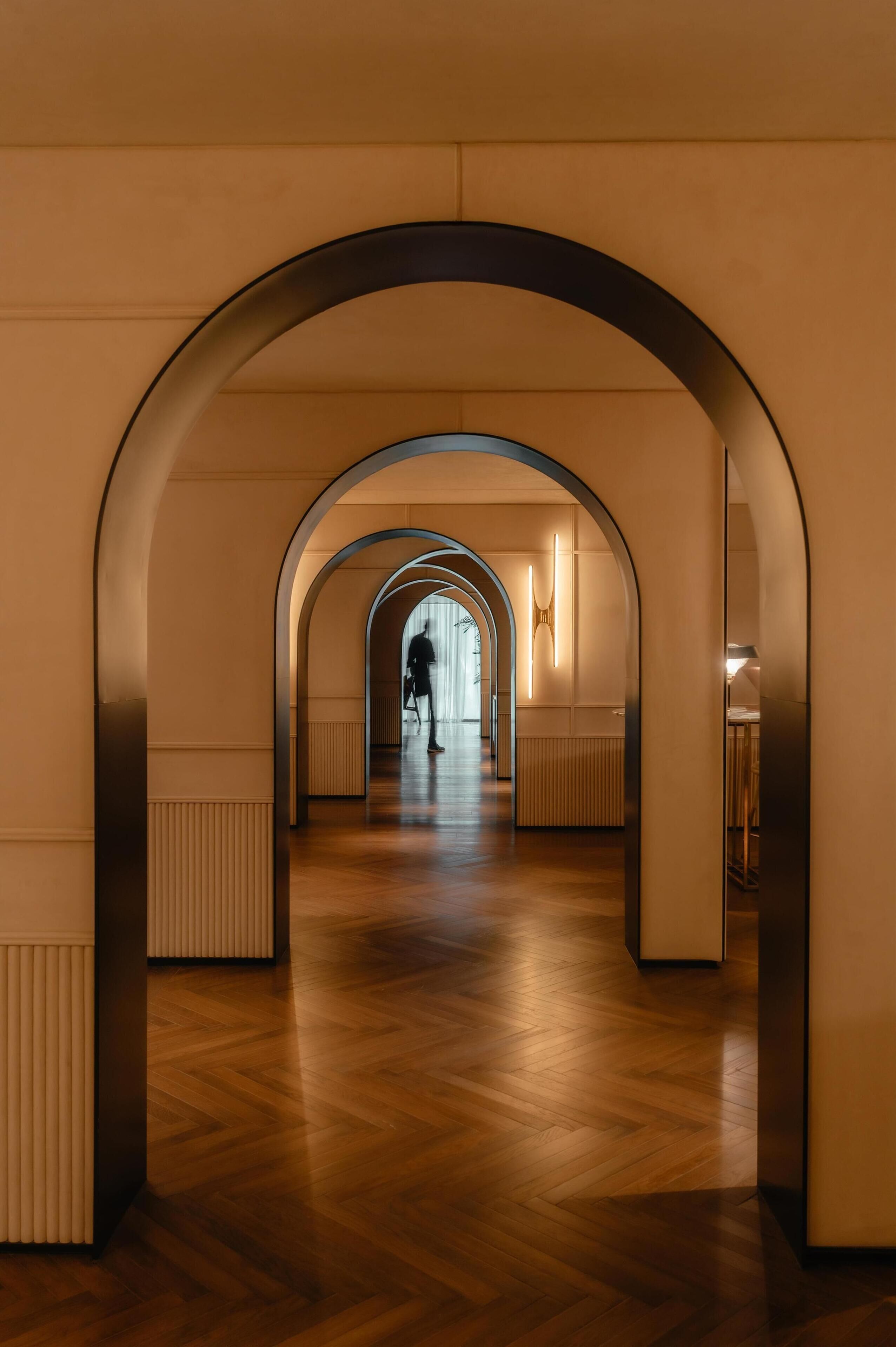 A corridor with wooden flooring and arched ceilings, leading to a room with a radiator and a wall-mounted light fixture.