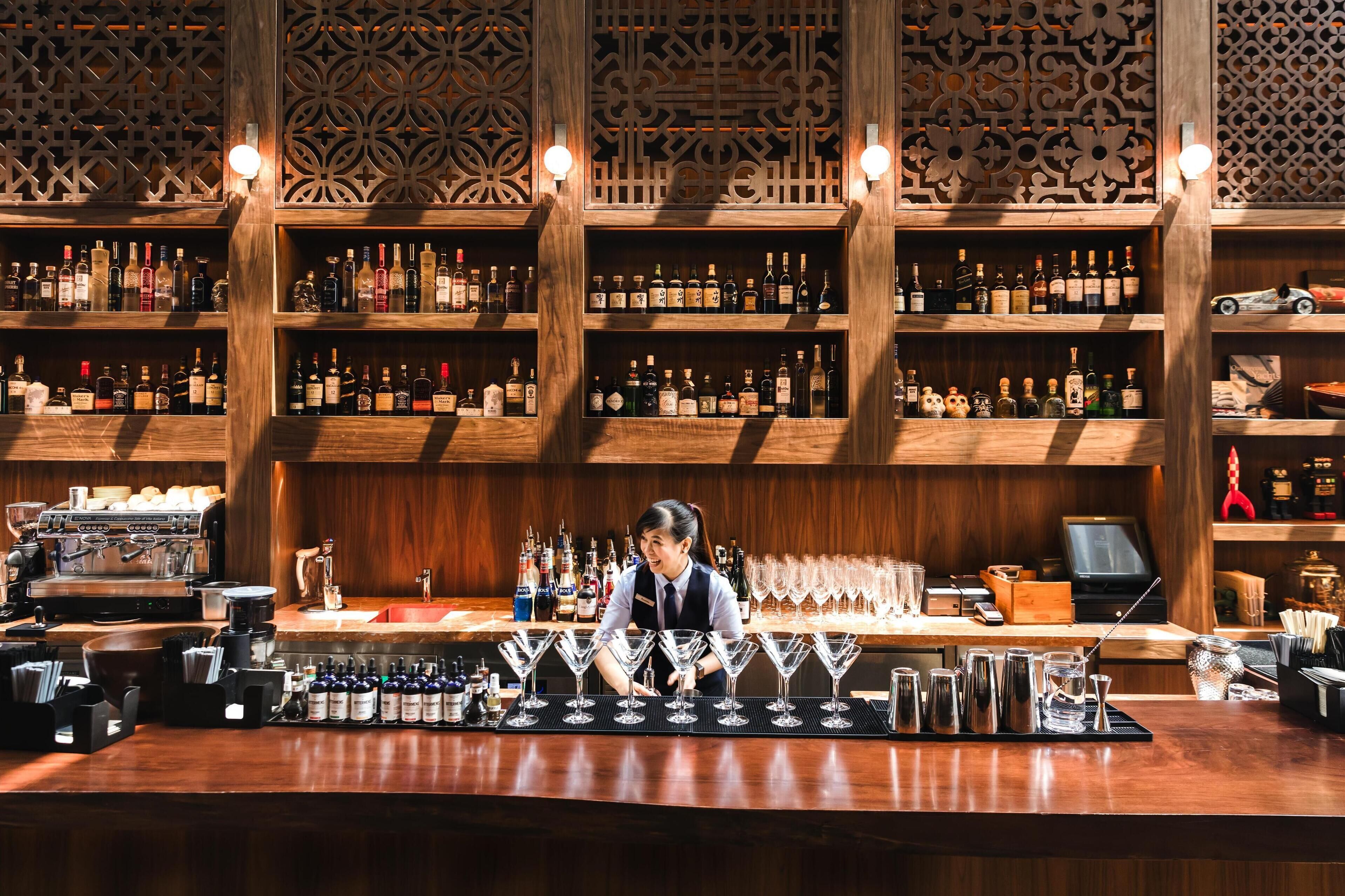 A bar area with shelves of liquor bottles, a bar counter with glasses, and a coffee machine.