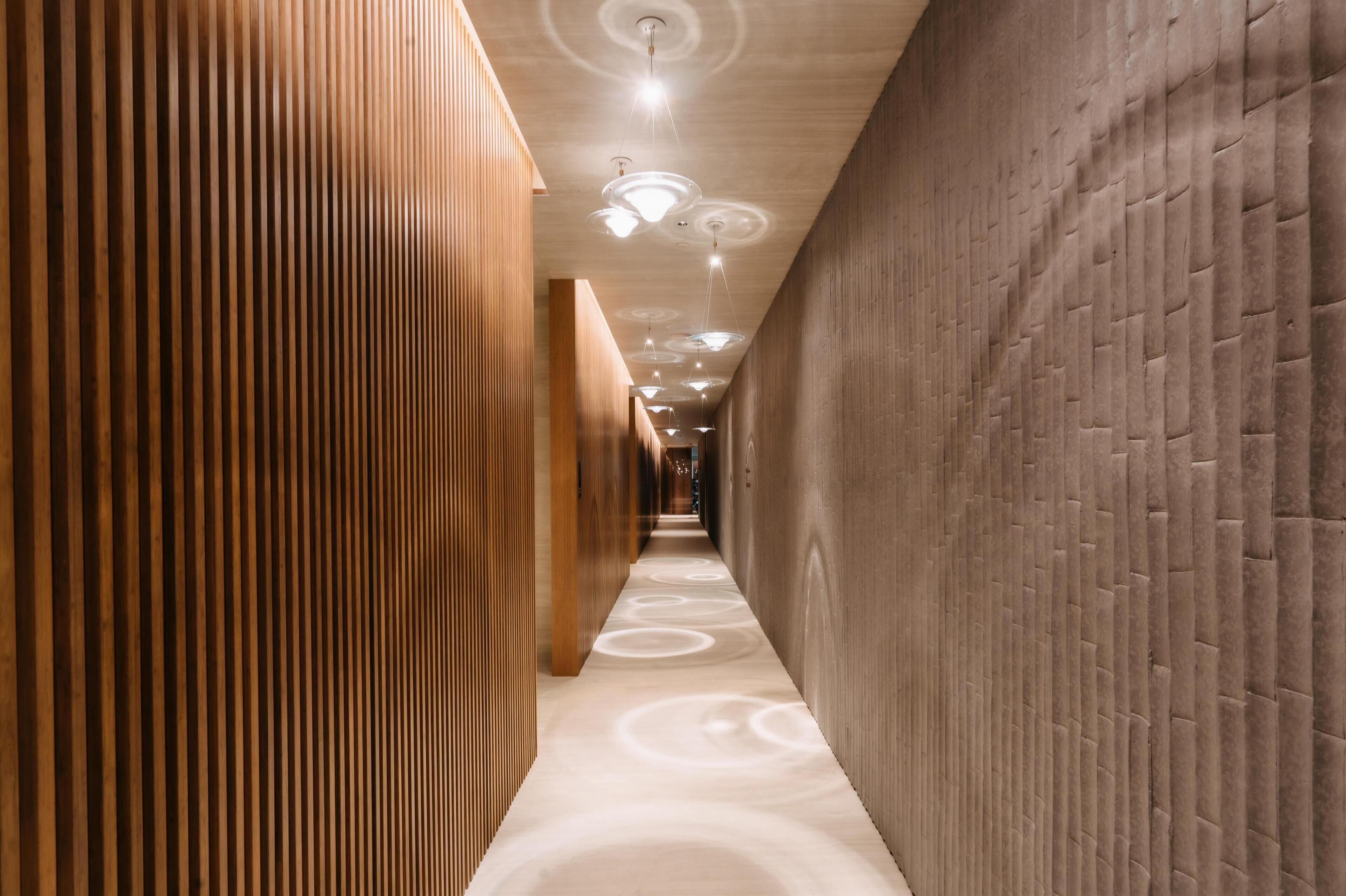 A modern hallway with wooden paneling and a textured wall, leading to a bright, circular light fixture on the ceiling.
