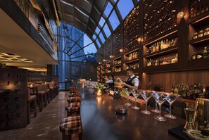 Un espace bar avec un long comptoir, des tabourets de bar et un barman qui prépare des boissons.