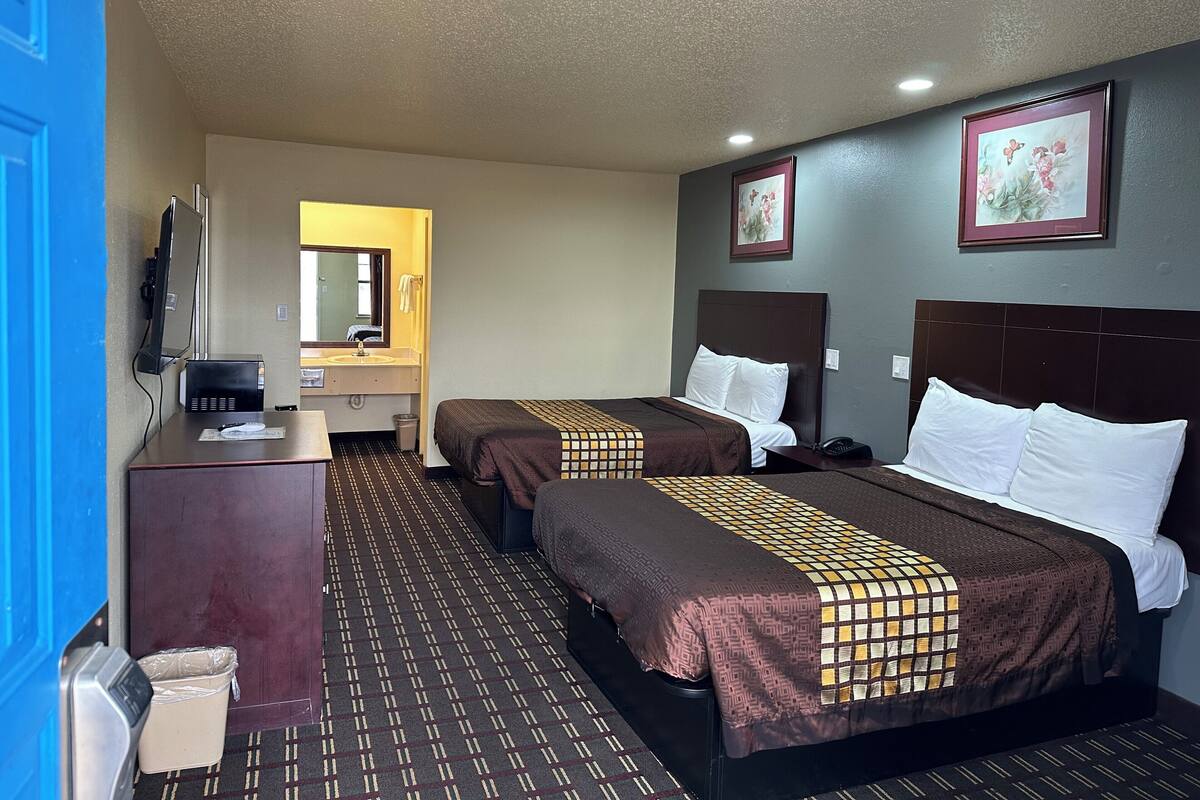 Habitación de hotel con dos camas, un escritorio, un espejo y un cesto de basura.