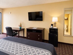 Una habitación de hotel con cama, escritorio, silla, televisor, lámpara y espejo.
