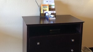 A dark wooden dresser with a flat-screen TV mounted above it. On the dresser, there is a box of Greater Prescott tissues and a book. - Executive Inn & Suites (Prescott)