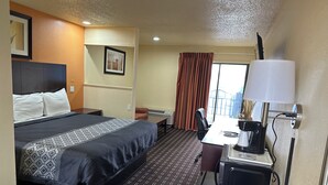 A hotel room with a bed, a desk with a lamp, a chair, a small table, and a window with curtains. - Executive Inn & Suites (Prescott)