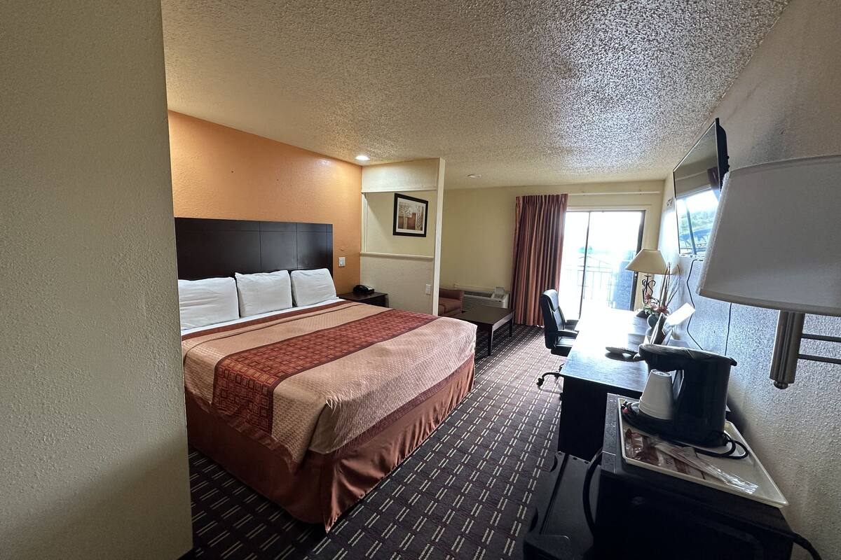 Habitación de hotel con cama, escritorio con lámpara, silla y vista al exterior.