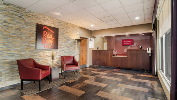 L’aire d’accueil d’un hôtel Red Roof Inn, avec un mur en pierre, deux chaises rouges, un comptoir d’accueil et un panneau indiquant que le Wi-Fi est gratuit dans toutes les chambres.