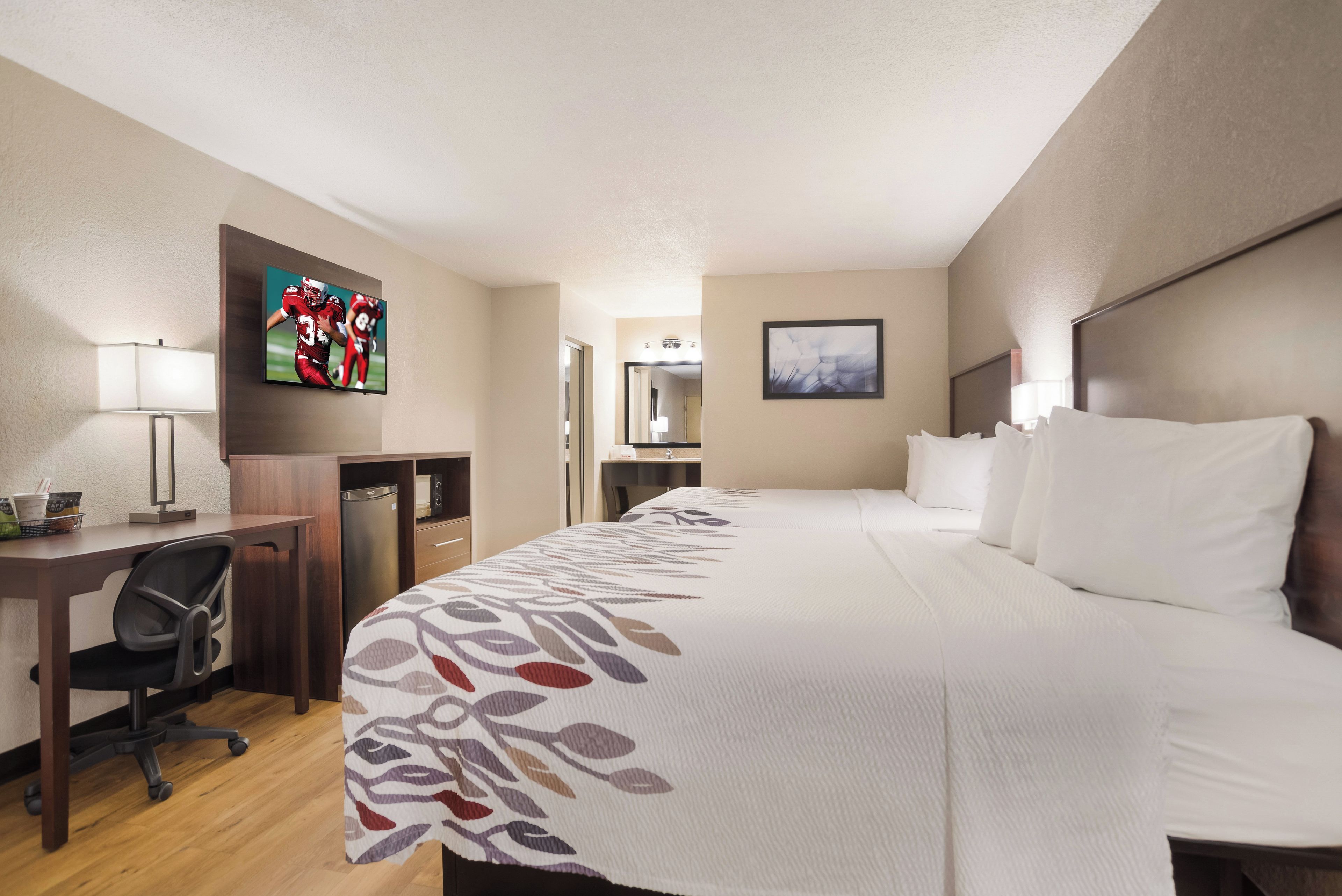 A hotel room with a bed, desk, chair, TV, and a bathroom.