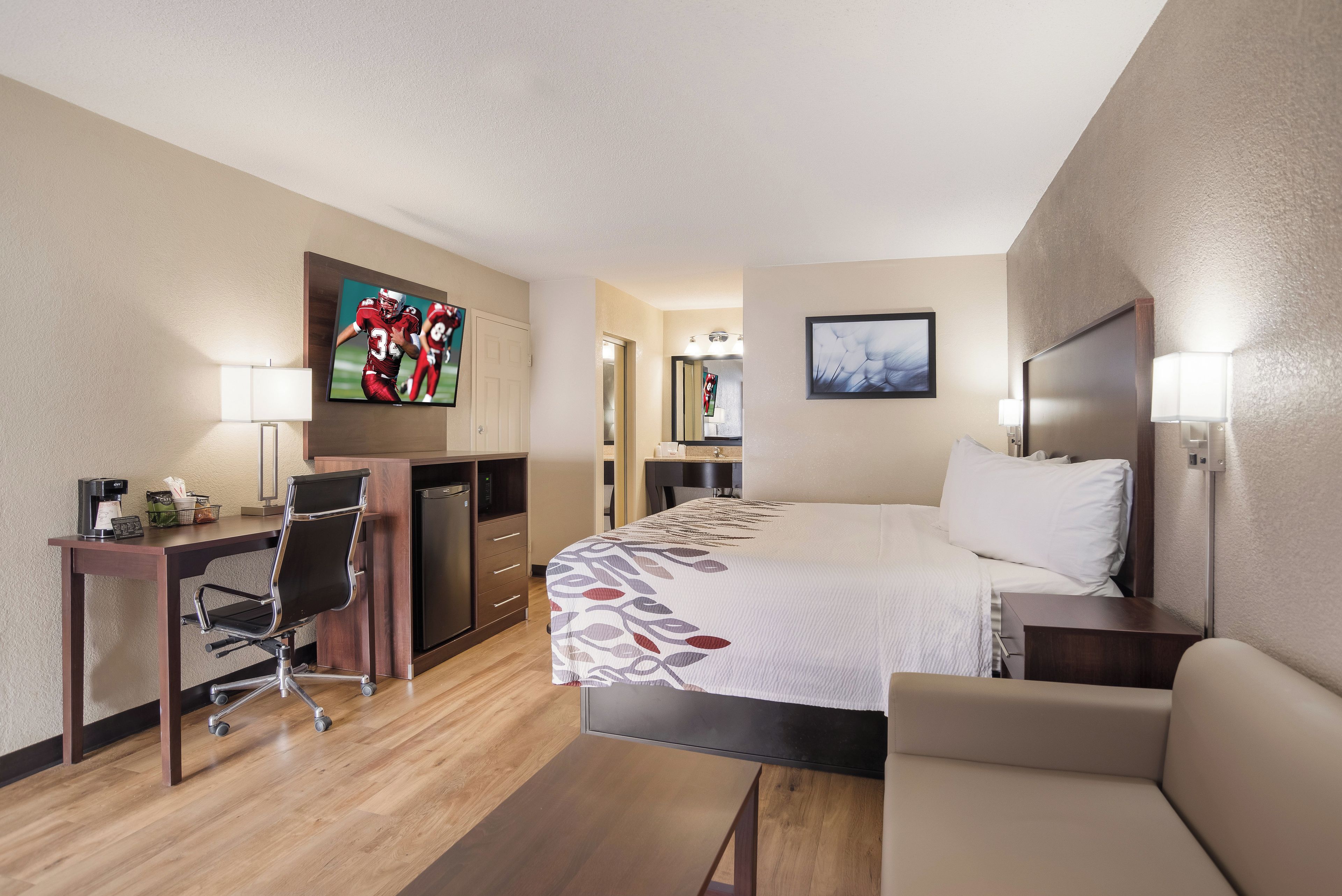 A hotel room with a bed, a desk with a chair, a television, and a bedside table.