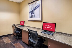 A hotel reception area with a computer desk, two chairs, a framed picture on the wall, and a sign indicating free Wi-Fi in all rooms.