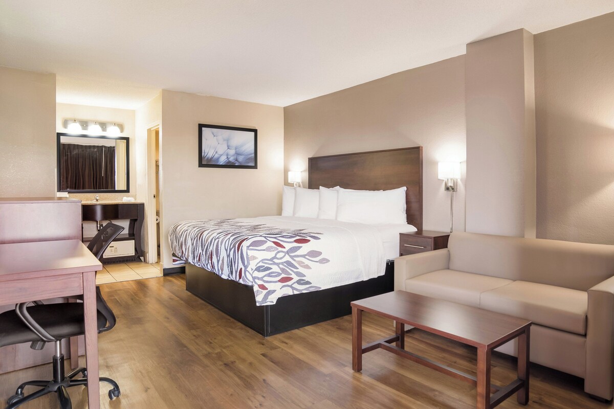 A hotel room with a bed, a desk, a chair, a sofa, and a bedside table.