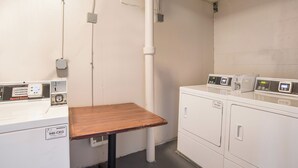 Une buanderie équipée de deux machines à laver, d’une table en bois et dont la tuyauterie est visible.