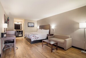 A hotel room with a bed, a desk, a chair, a sofa, and a bedside table.