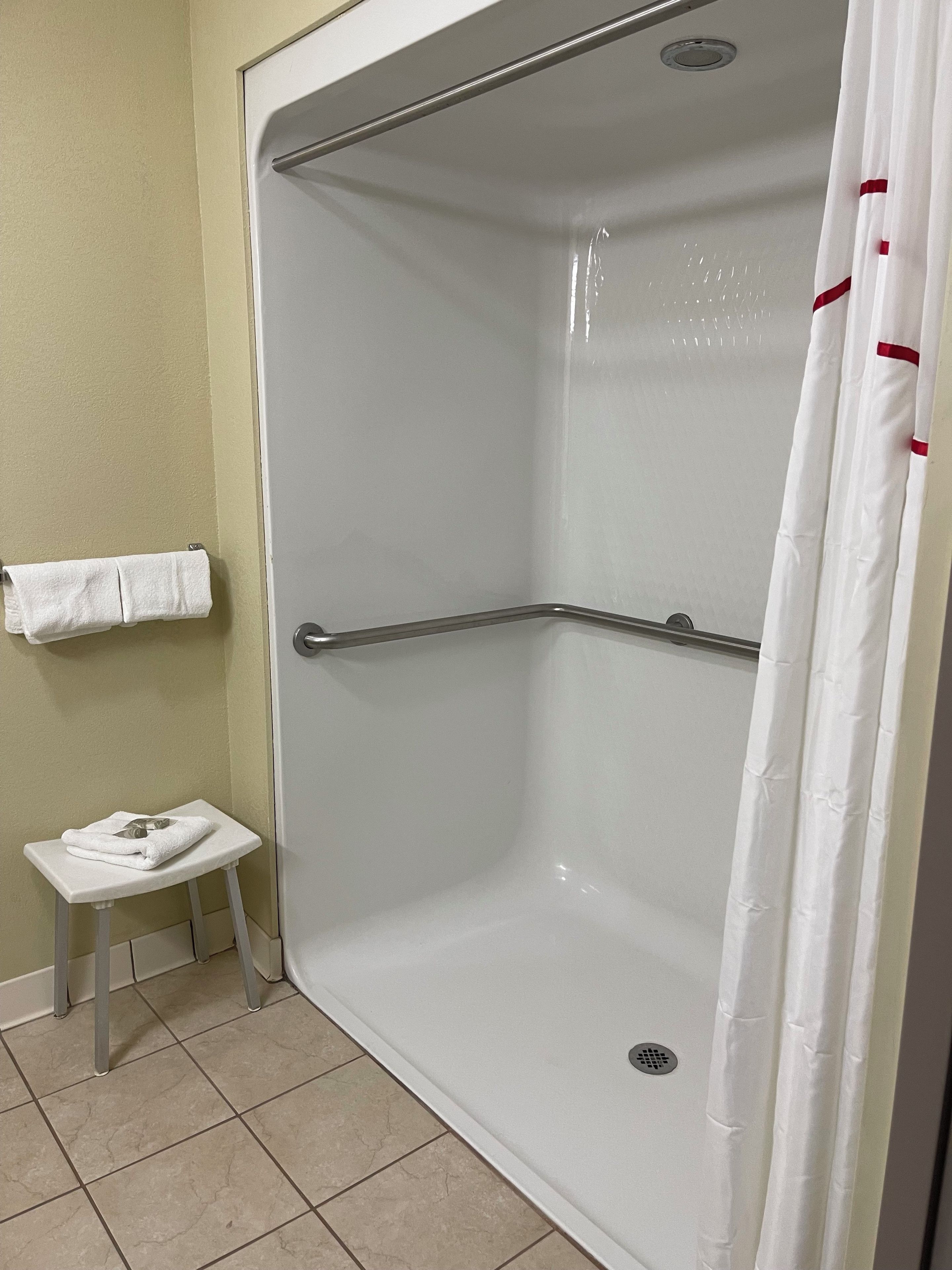 A shower area with a white tiled floor, a white towel on a small stool, and a shower curtain.