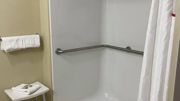 A shower area with a white tiled floor, a white towel on a small stool, and a shower curtain.