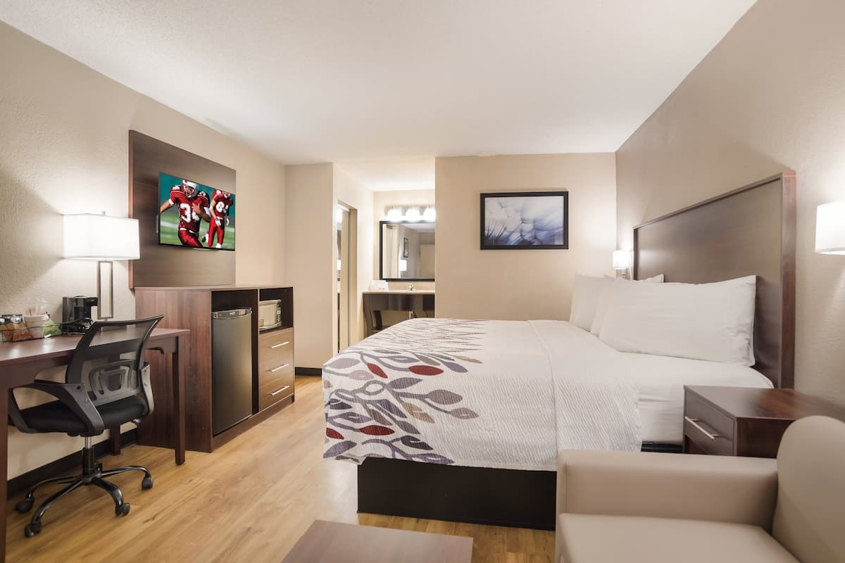 A hotel room with a bed, desk, chair, and a television.