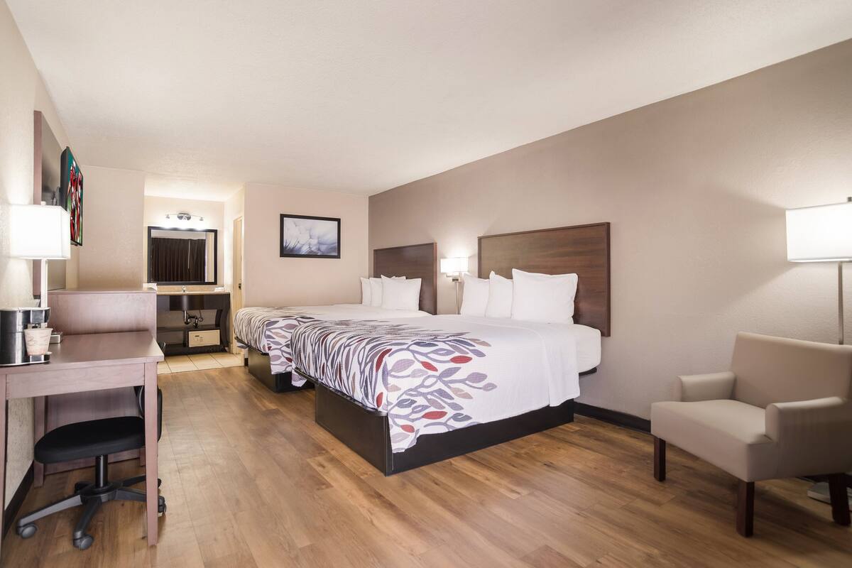 A hotel room with a bed, desk, chair, and a bathroom with a mirror.