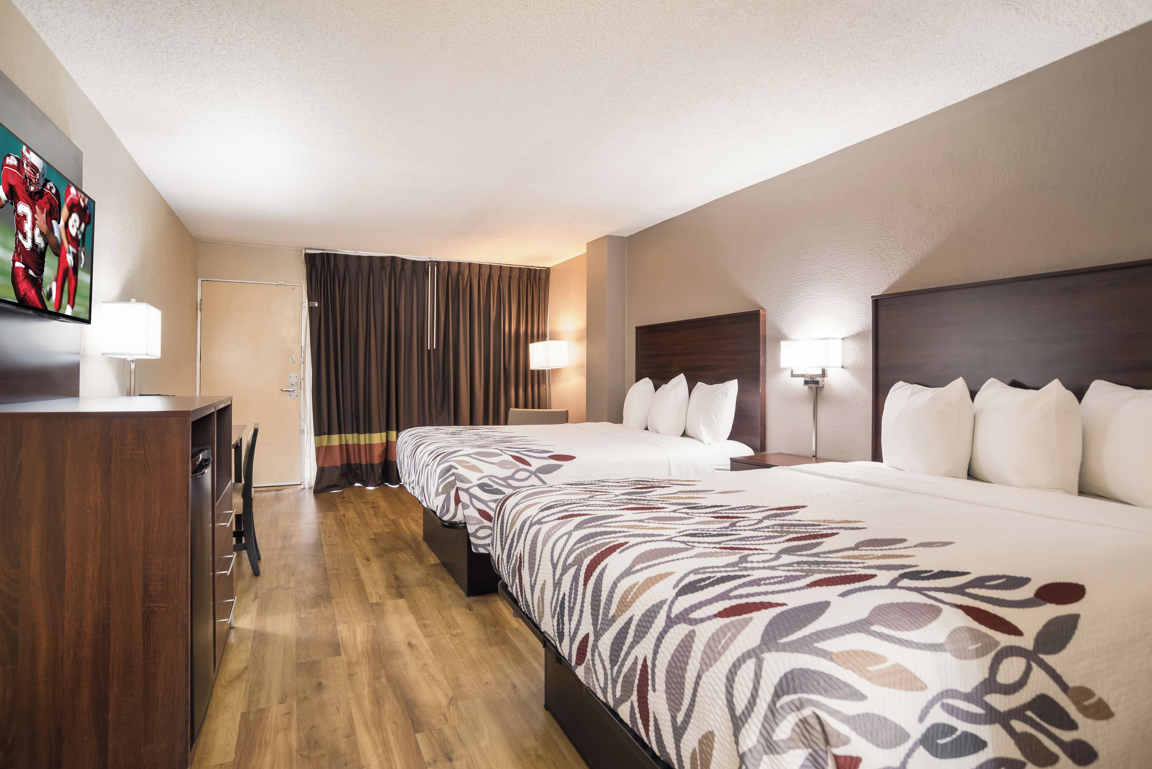 Habitación de hotel con una cama grande, un escritorio, un televisor y una cortina.