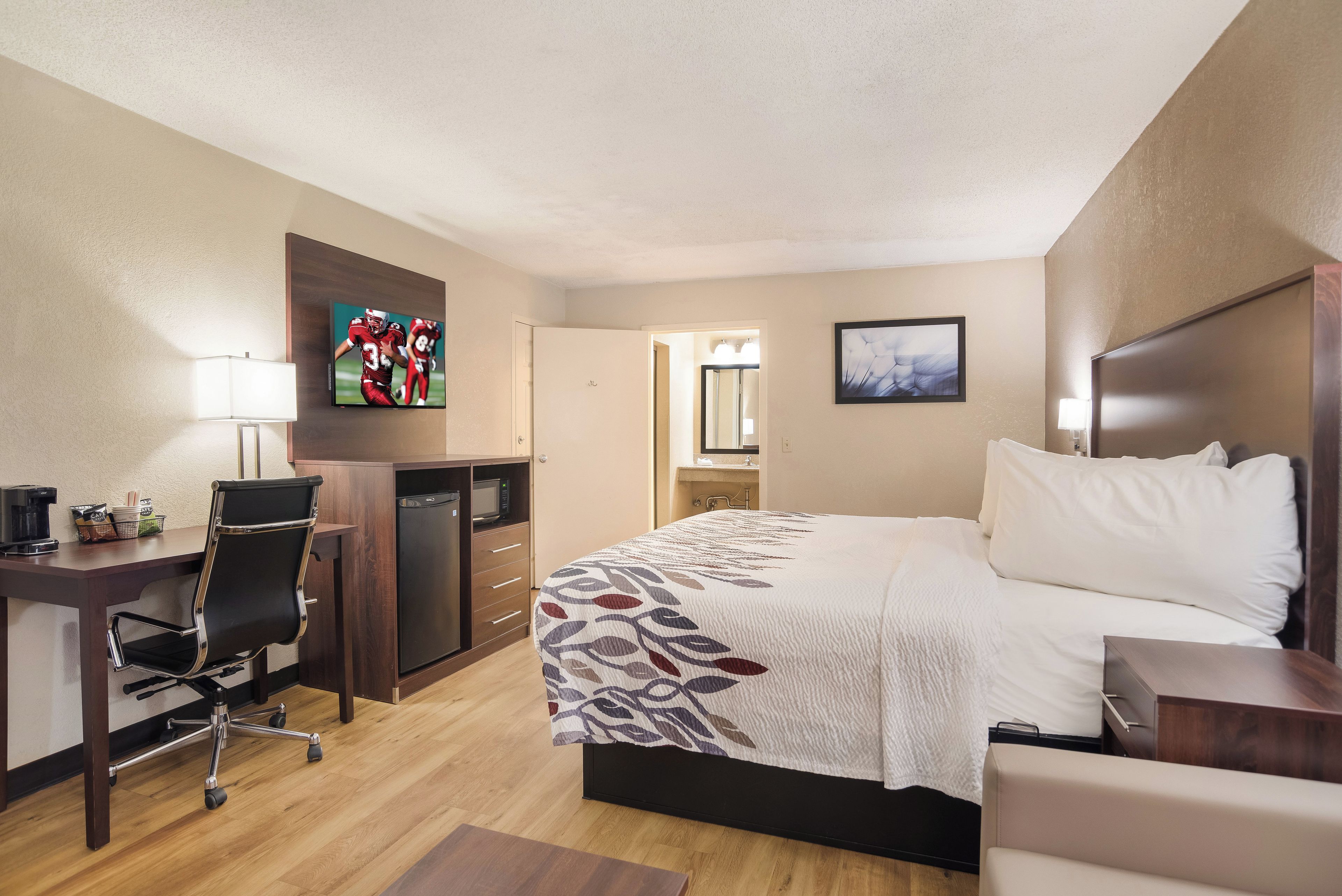 A hotel room with a bed, desk, chair, television, and a bathroom visible through an open door.