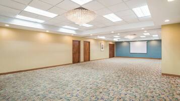 A spacious room with patterned carpet, wooden doors, a chandelier, and a projector screen on the wall.