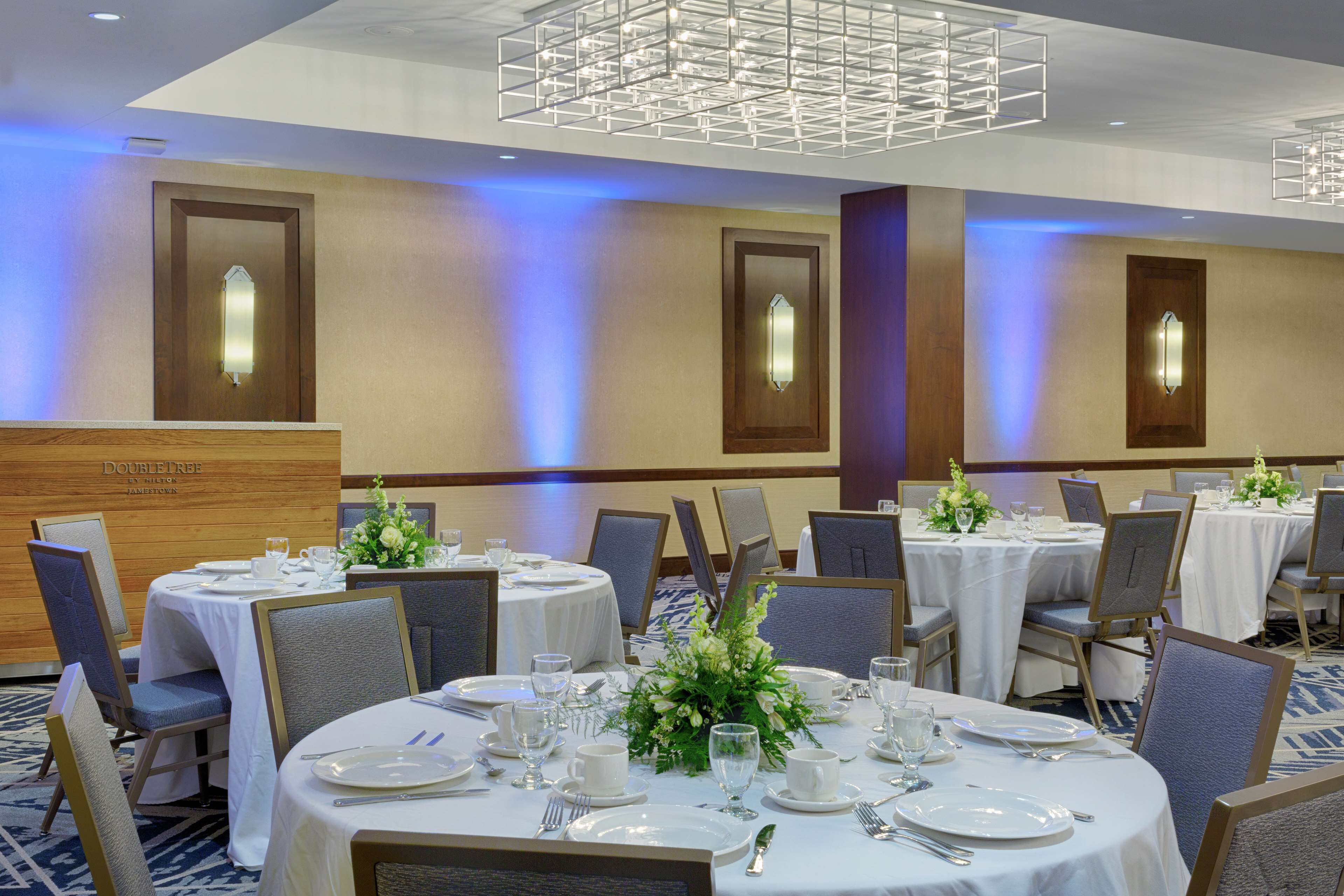 Une salle de banquet avec des tables rondes dressées pour le repas, chacune étant recouverte d’une nappe blanche et agrémentée de chaises et de décorations de table.