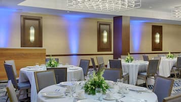 A banquet hall with round tables set for dining, each with white tablecloths, chairs, and centerpieces.